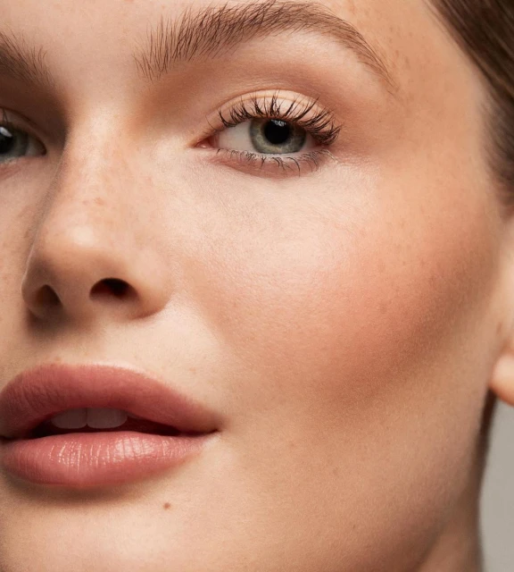 Close-up portrait of a woman's face with fair skin, showcasing natural makeup and soft, diffused lighting in a beauty context.