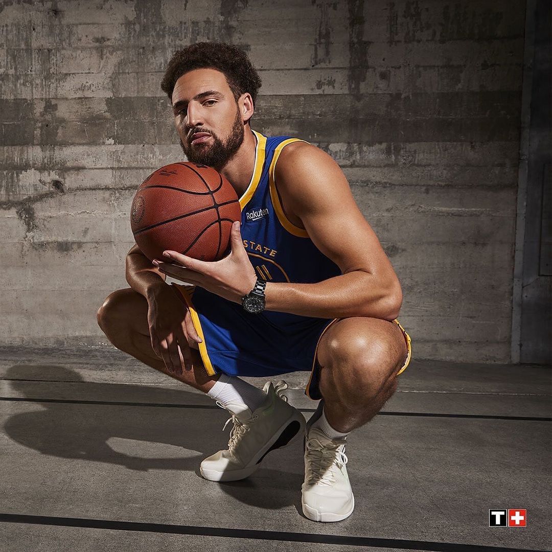 Professional portrait of a basketball player in a blue and gold jersey holding a basketball in a photo studio with a grey background.