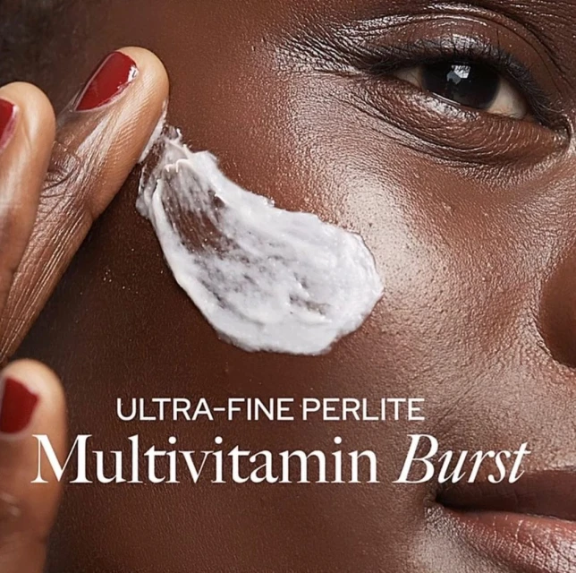 Close-up of a dark-skinned adult female applying a white cream product to her cheek, showcasing skincare or beauty product advertisement.