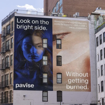 Outdoor advertising featuring a split-face beauty advertisement on a building wall, with text promoting skin protection and the brand 'pavise'.