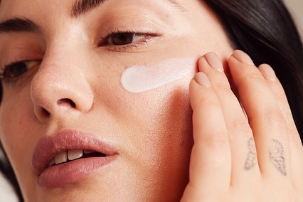 Close-up of a person applying cream to their cheek. Focus on the light-skinned human face with visible fingers and hand. Beauty concept.