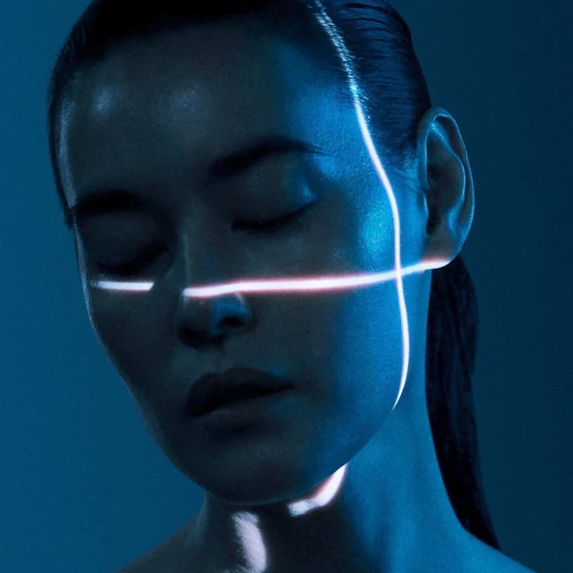 Adult woman's face in close-up with closed eyes under strong blue light and glowing white lines. Beauty and visual effects concept.