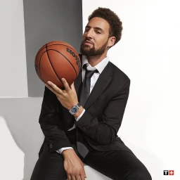 Man wearing a black suit and tie holding a basketball against a white and grey studio background.