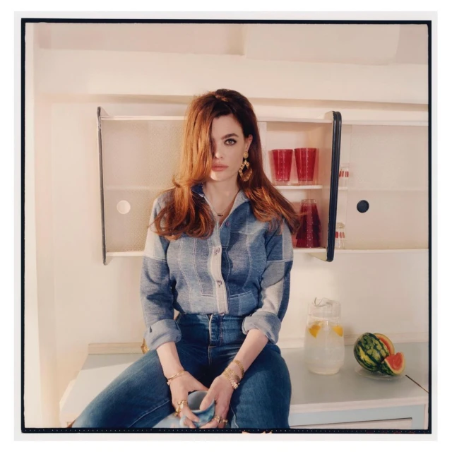 Woman with long auburn hair and blue eyes poses indoors wearing a denim shirt and jeans, next to a pitcher of lemonade and watermelon.