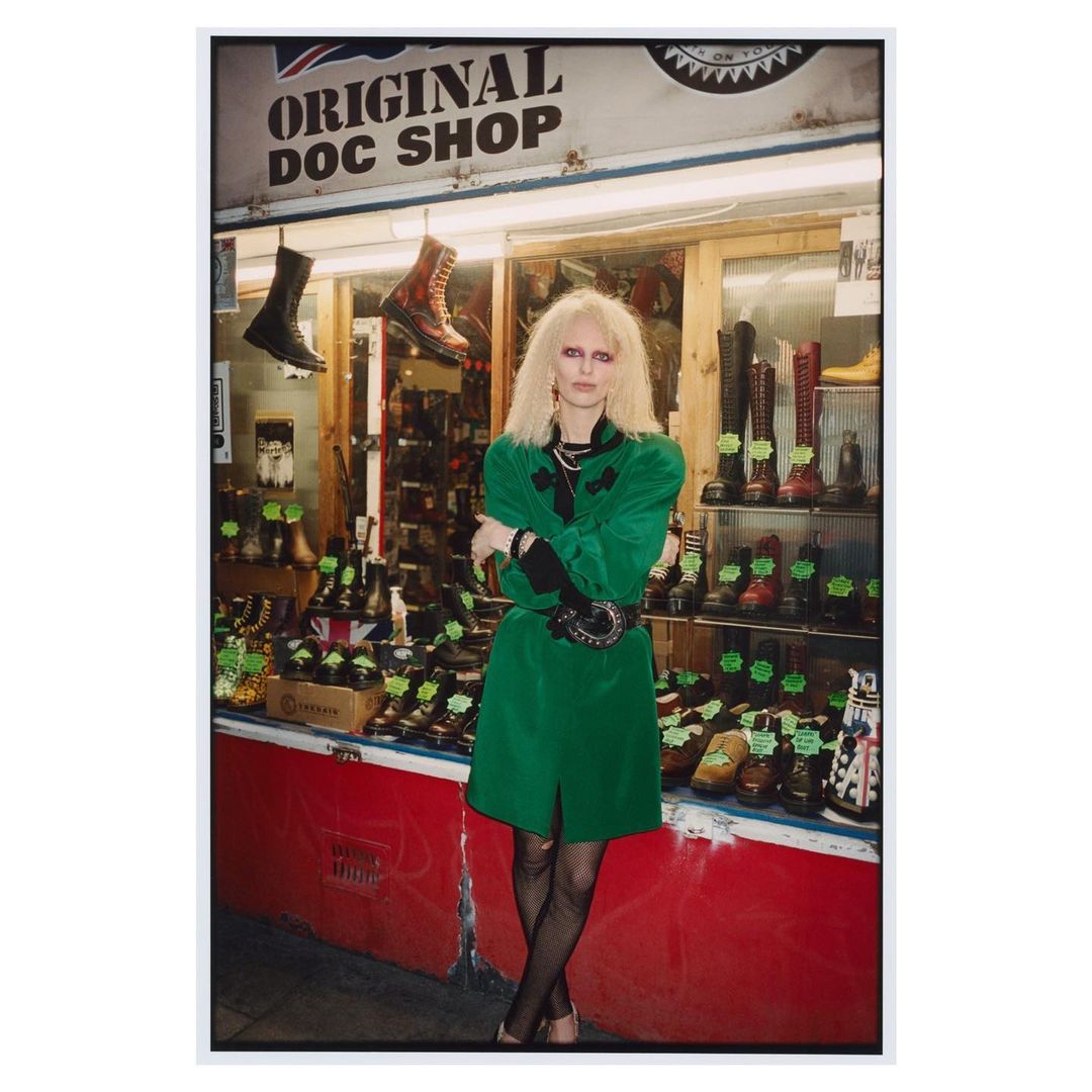 Woman in green coat standing in front of Original Doc Shop with a window display of Dr. Martens boots and shoes.
