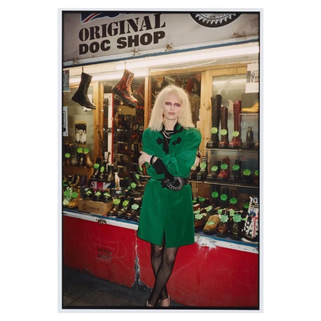 Woman in green coat standing in front of Original Doc Shop with a window display of Dr. Martens boots and shoes.