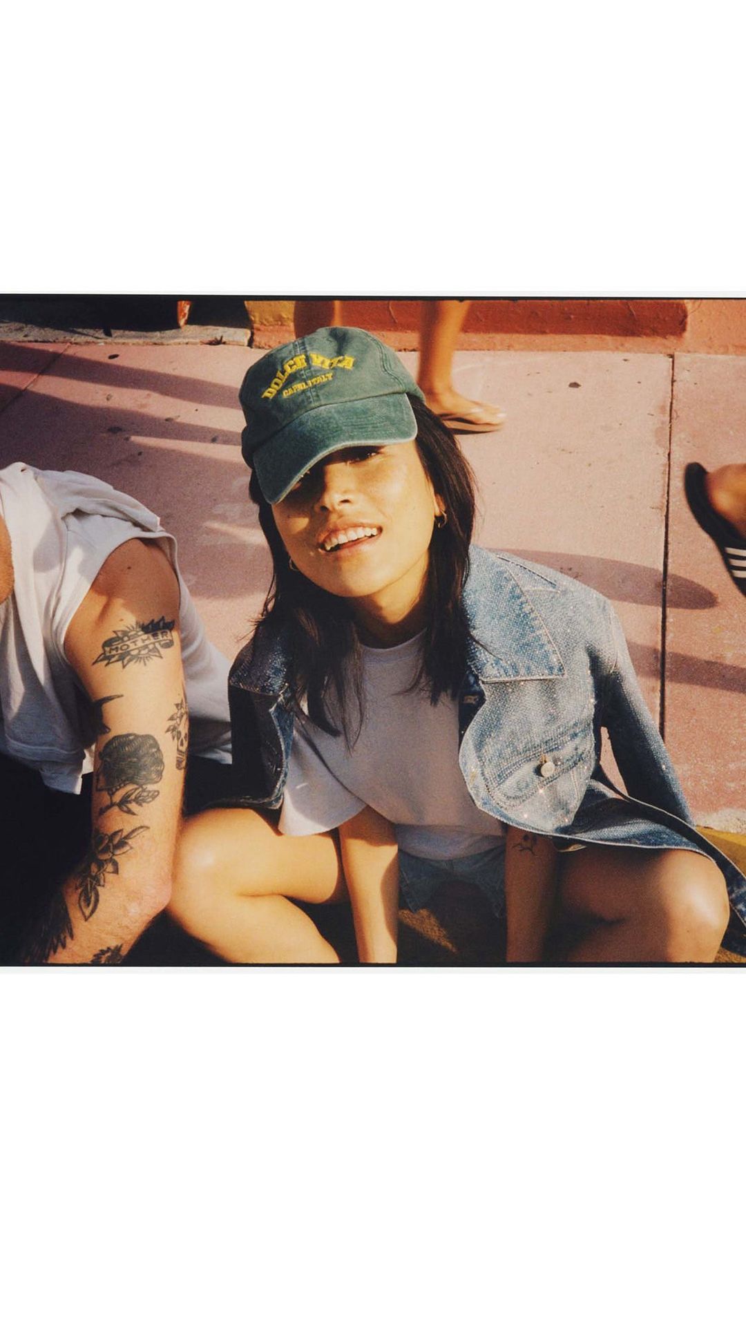 Candid shot of a young woman wearing a denim jacket and green baseball cap outdoors in London by Tom Craig.
