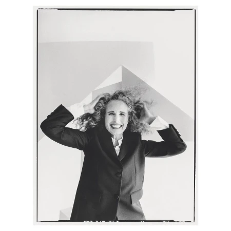 Monochrome portrait of a smiling woman with curly hair wearing a dark suit jacket against a white studio background.