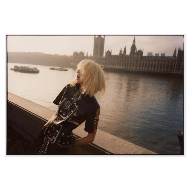 Woman in a printed dress stands on a bridge in London with the Houses of Parliament in the background, overlooking the River Thames.