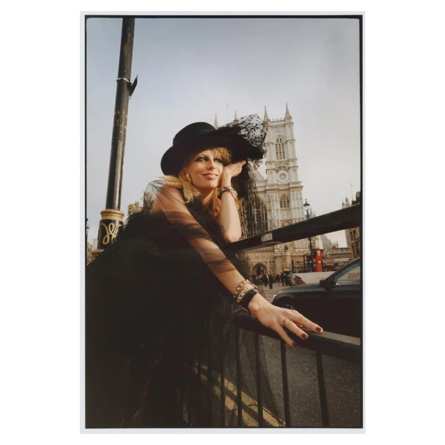 Woman in black hat and dress leaning on railing with Westminster Abbey in the background, fashion editorial, outdoor daylight shot.