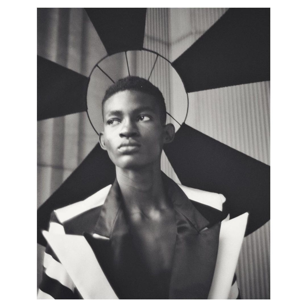 Striking monochrome portrait of a young man in a blazer, gazing off-camera, with a geometric backdrop creating a unique halo effect.