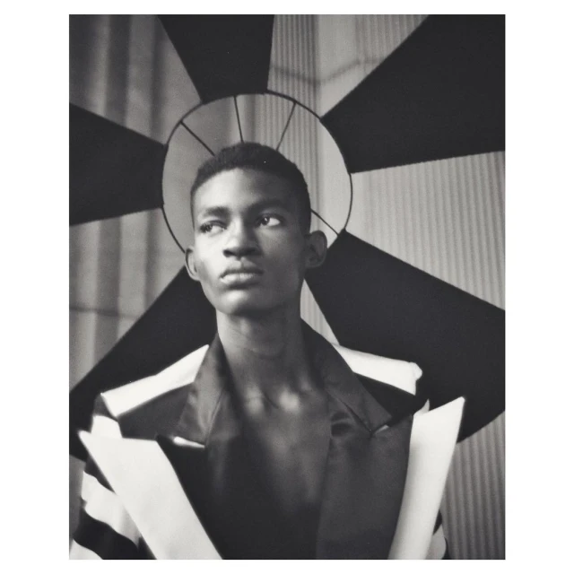 Striking monochrome portrait of a young man in a blazer, gazing off-camera, with a geometric backdrop creating a unique halo effect.