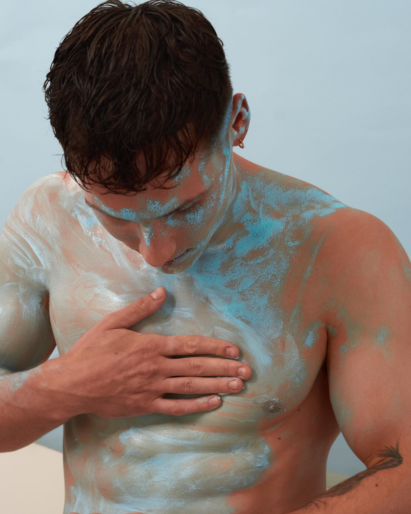 Shirtless man with blue body paint. Close-up shot in a studio. The man is touching his chest with his right hand. Fitness concept.