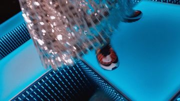 Aerial shot of a person in sparkling dress and colorful sneakers walking on an illuminated blue platform, with mirrored background, overhead.