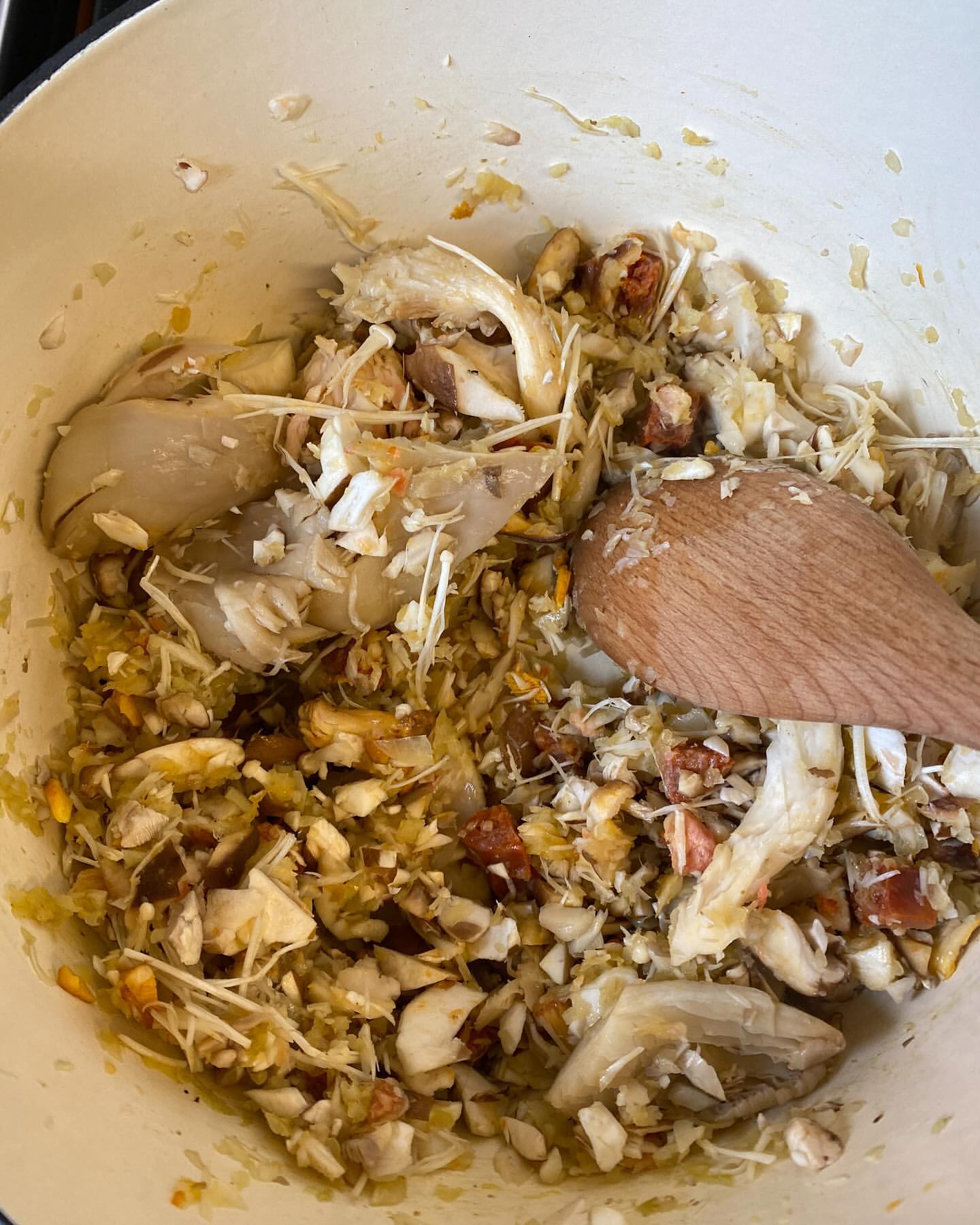 Close-up of crab filling in a pot with visible wooden spoon. A mix of crab meat, vegetables and sauce being prepared in the kitchen.