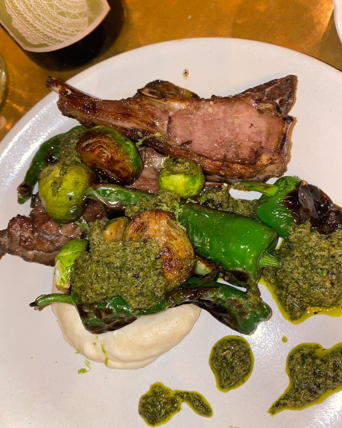 Overhead shot of a gourmet lamb chop dish with brussel sprouts, peppers, and a creamy sauce, showcasing food presentation and dining.