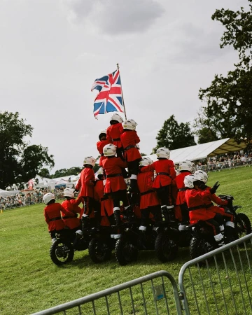Acrobatic display featuring a large group of people on motorcycles forming a pyramid on green grass beneath the Union Jack.