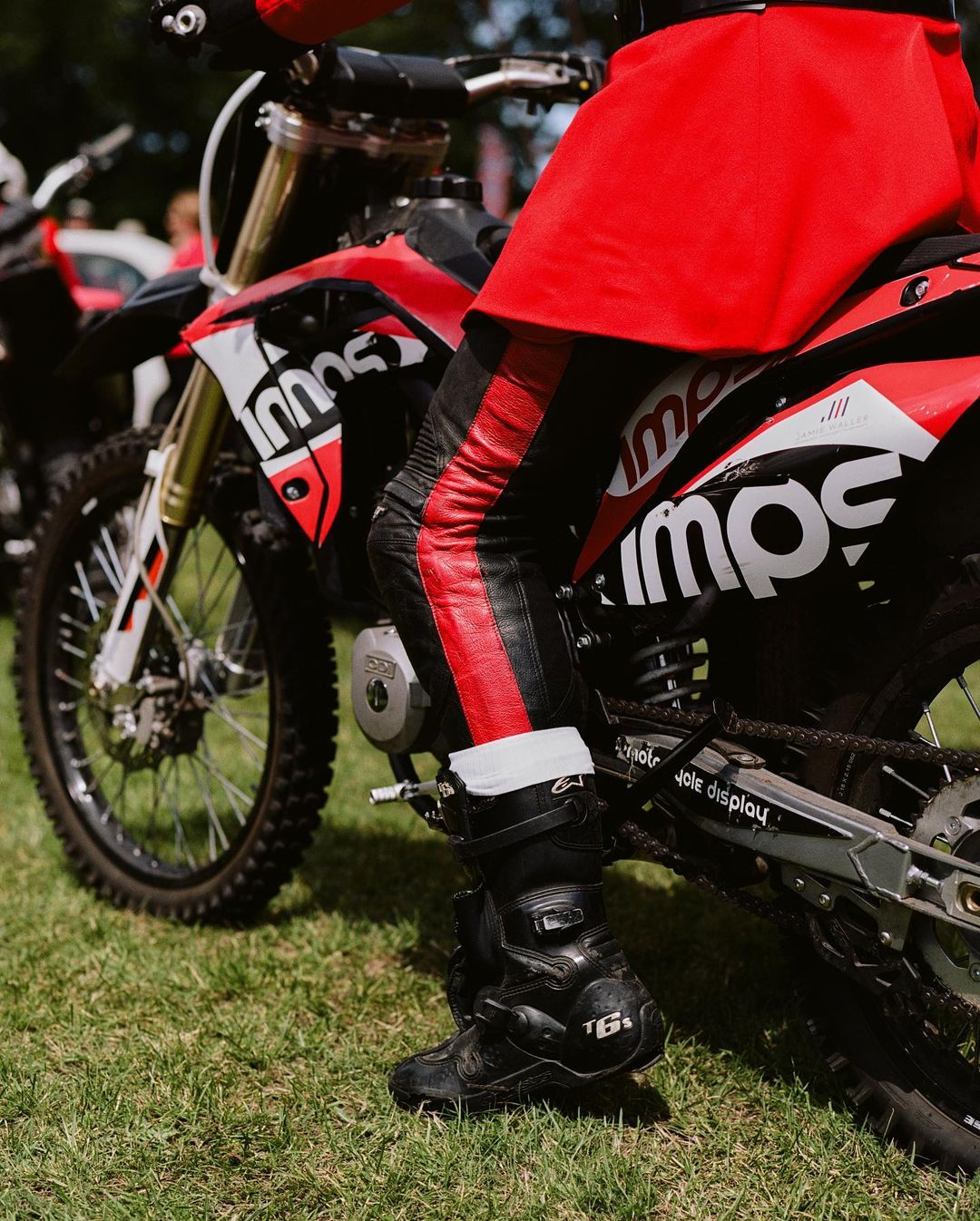 Red and black dirt bike with a rider wearing matching gear on a grassy surface, capturing a moment in an outdoor setting.