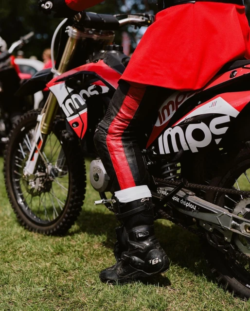 Red and black dirt bike with a rider wearing matching gear on a grassy surface, capturing a moment in an outdoor setting.
