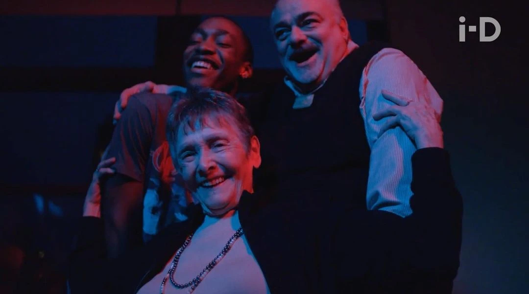 Three adults smiling at the camera in a dimly lit area with red and blue lighting.