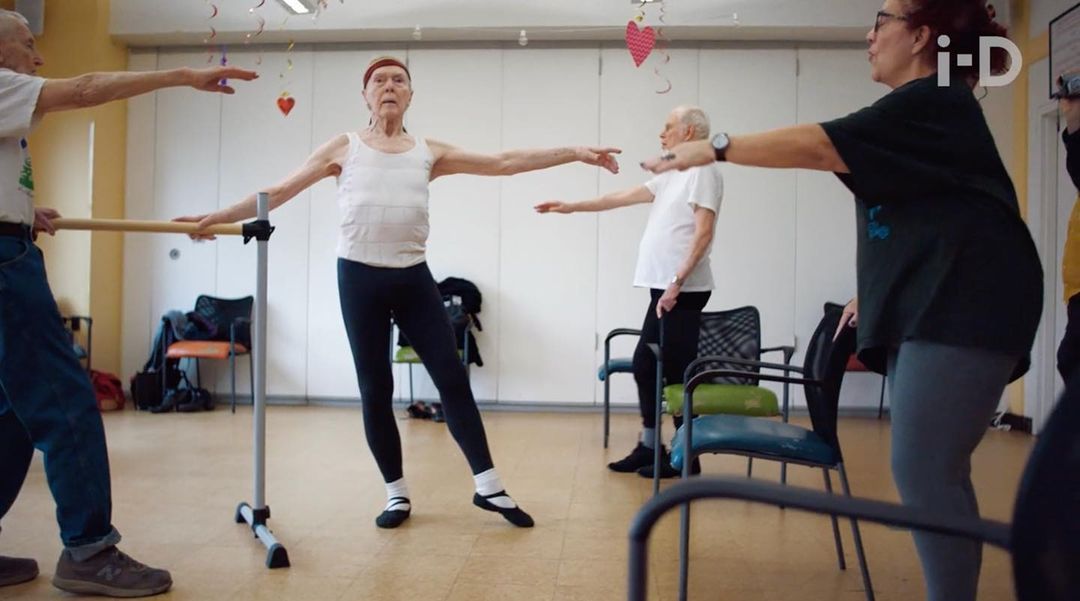 Group of senior adults in dance studio, practicing ballet with barre. Elderly people in exercise class, wearing casual clothing. 