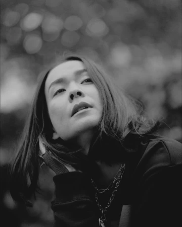 Monochrome portrait of a woman looking upward outdoors with soft blurred foliage in the background
