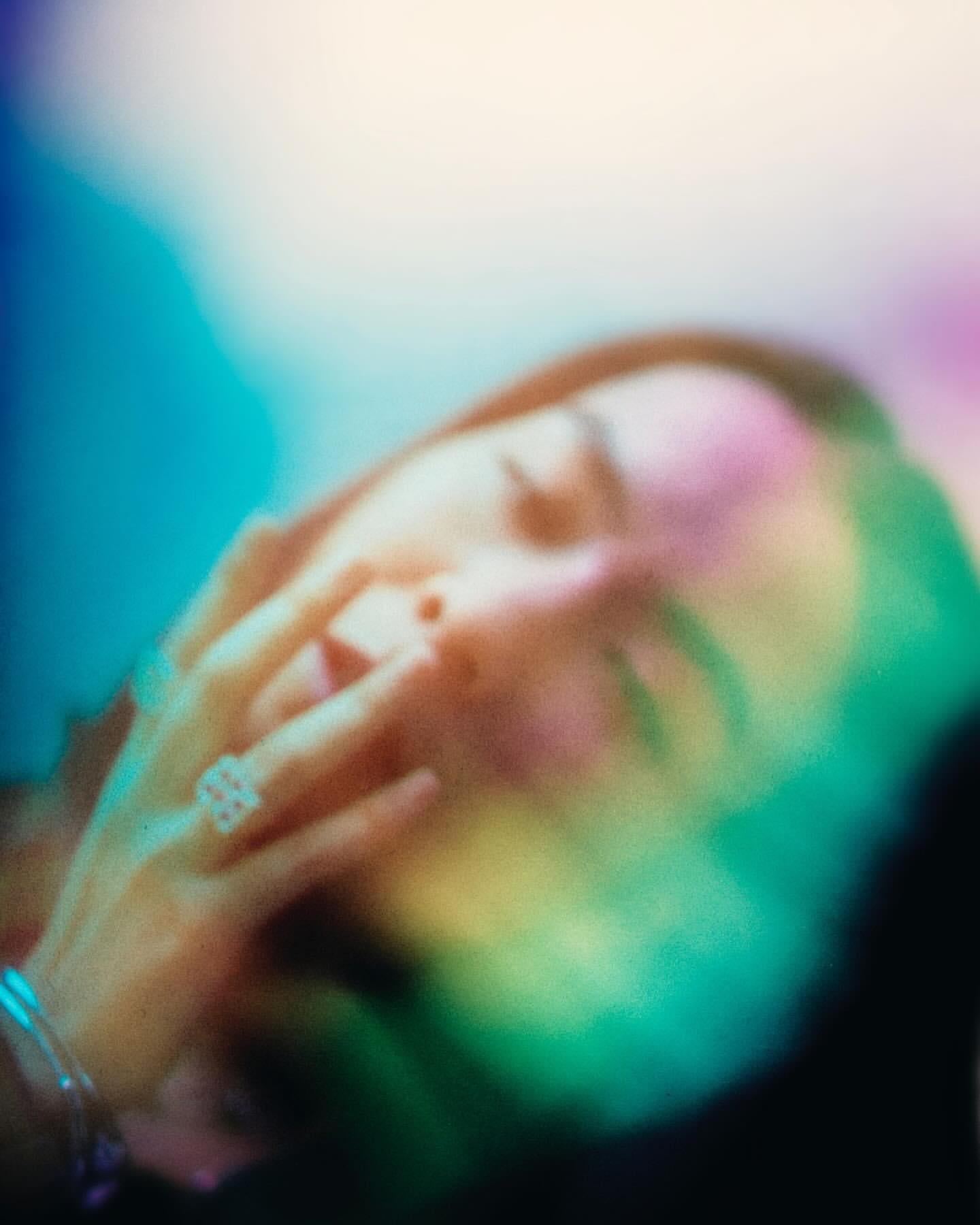 Close-up portrait of a woman with her hand near her face, bathed in colorful prismatic light flares against a dark background.