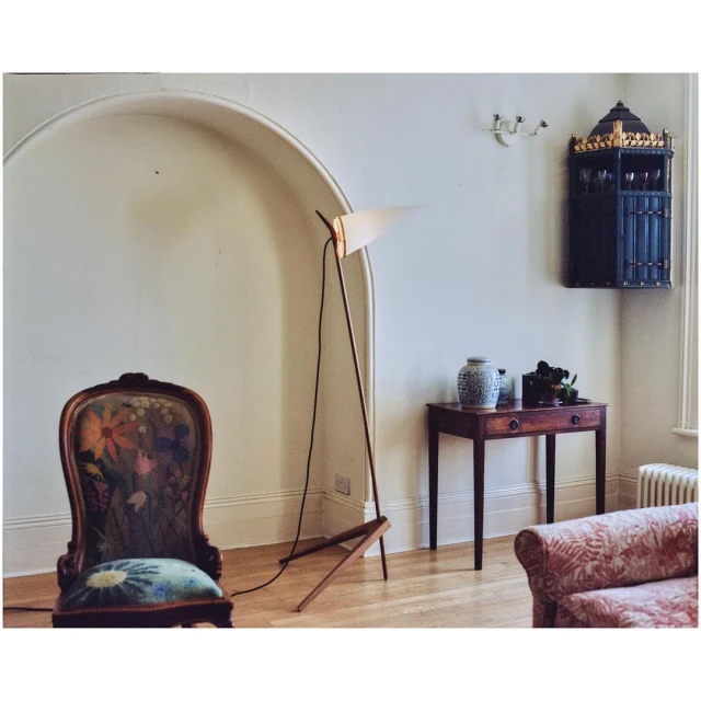 Interior view of living room with vintage chair with floral pattern, modern floor lamp, and antique-style side table with blue and white vase.
