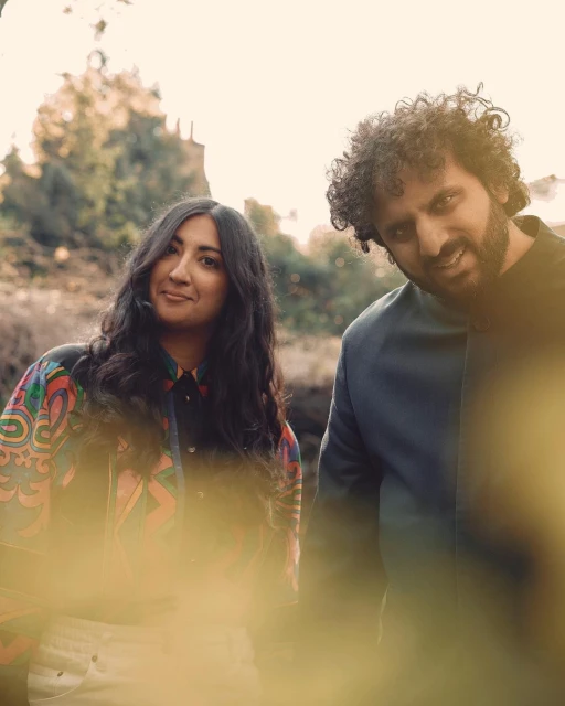 Couple in outdoor setting featuring an adult woman with long dark hair and an adult man with curly dark hair, wearing fashionable jackets.