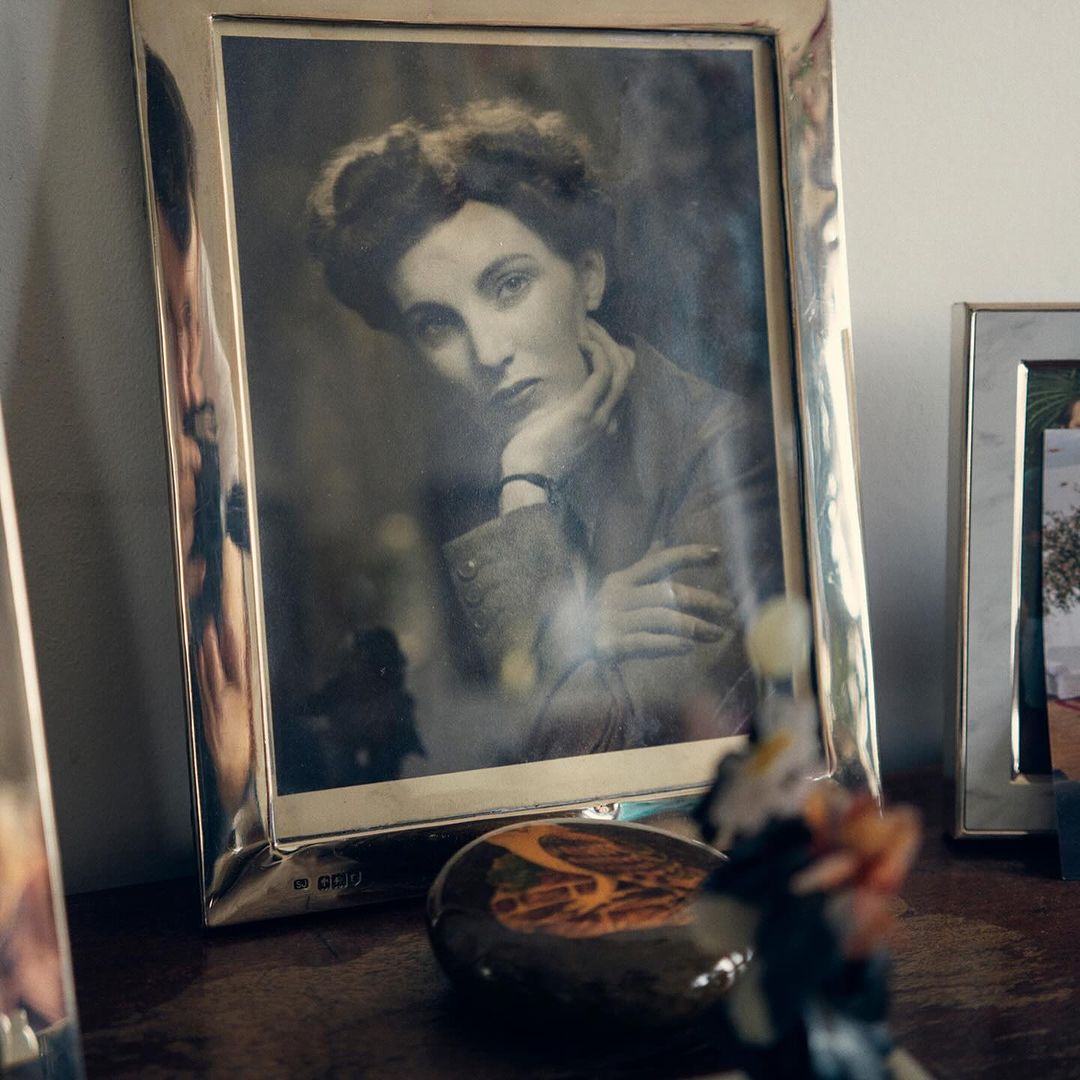Vintage photo of a woman in a silver frame on a wooden table with a decorative stone and other framed images, creating a nostalgic atmosphere.