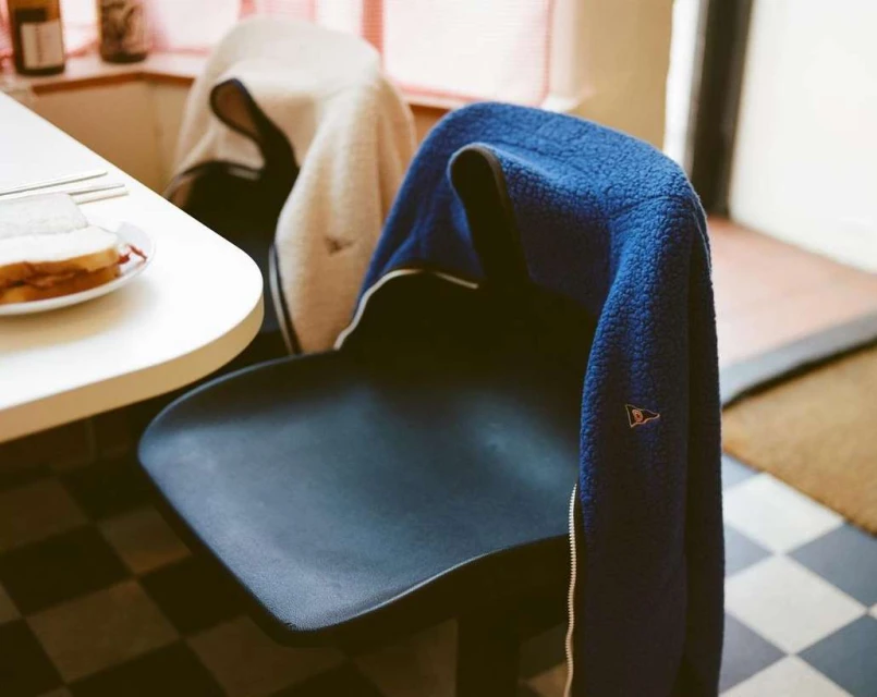 Indoor view featuring a blue fleece jacket draped on a black chair next to a table set with a plate of sandwiches.
