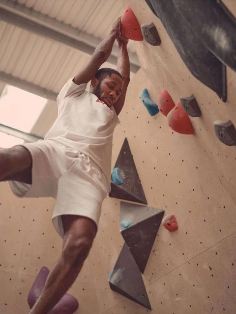 Athletic man in white clothing rock climbs indoors on a climbing wall with handholds. Sport and fitness concept. Eye-level angle.