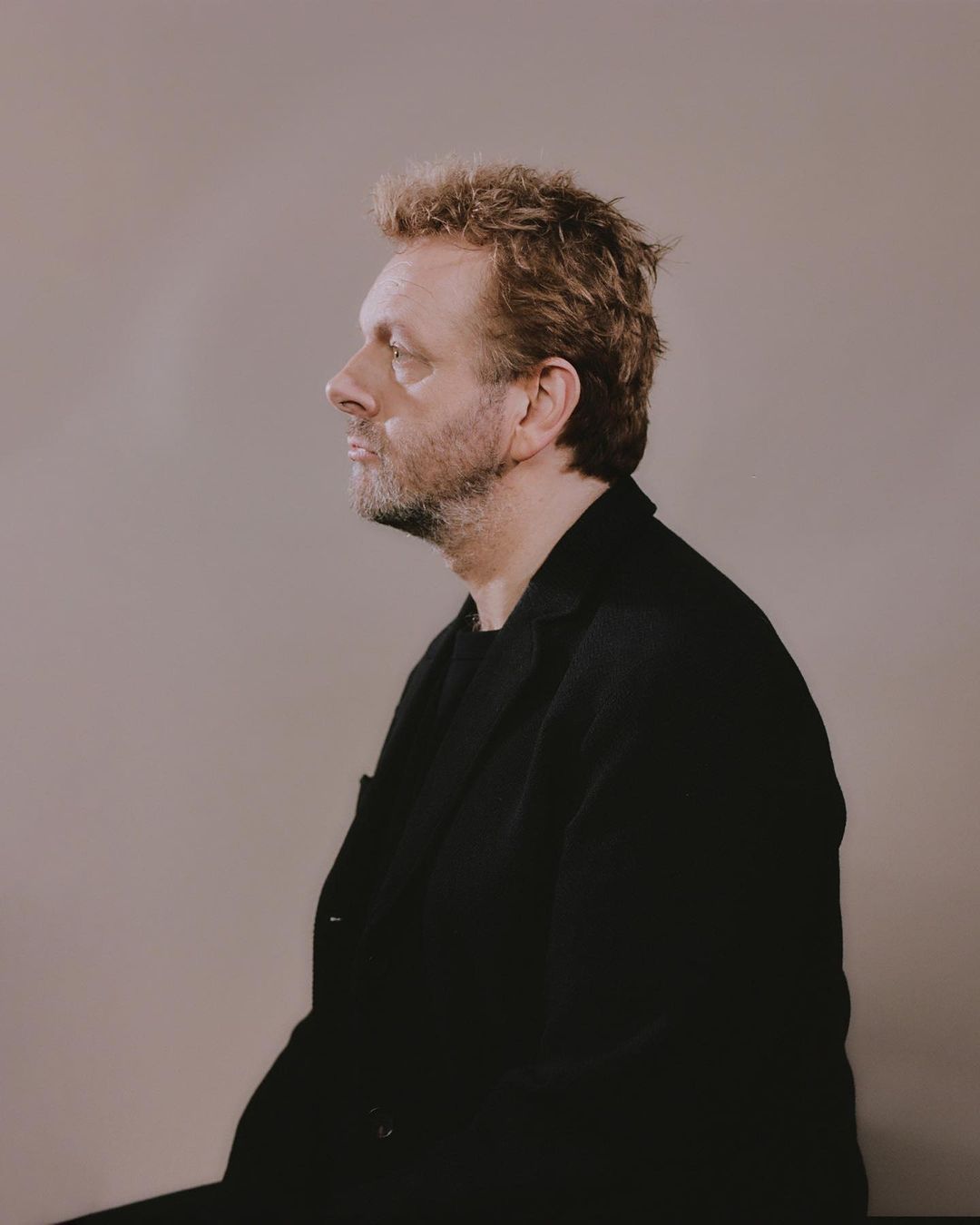 Side profile portrait of a middle-aged man with curly hair wearing a black jacket against a neutral background in a photo studio.