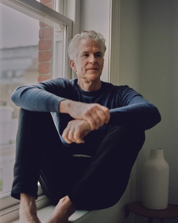 Older man with grey hair wearing a blue sweater seated in a window frame photographed by Tom Jamieson in New York