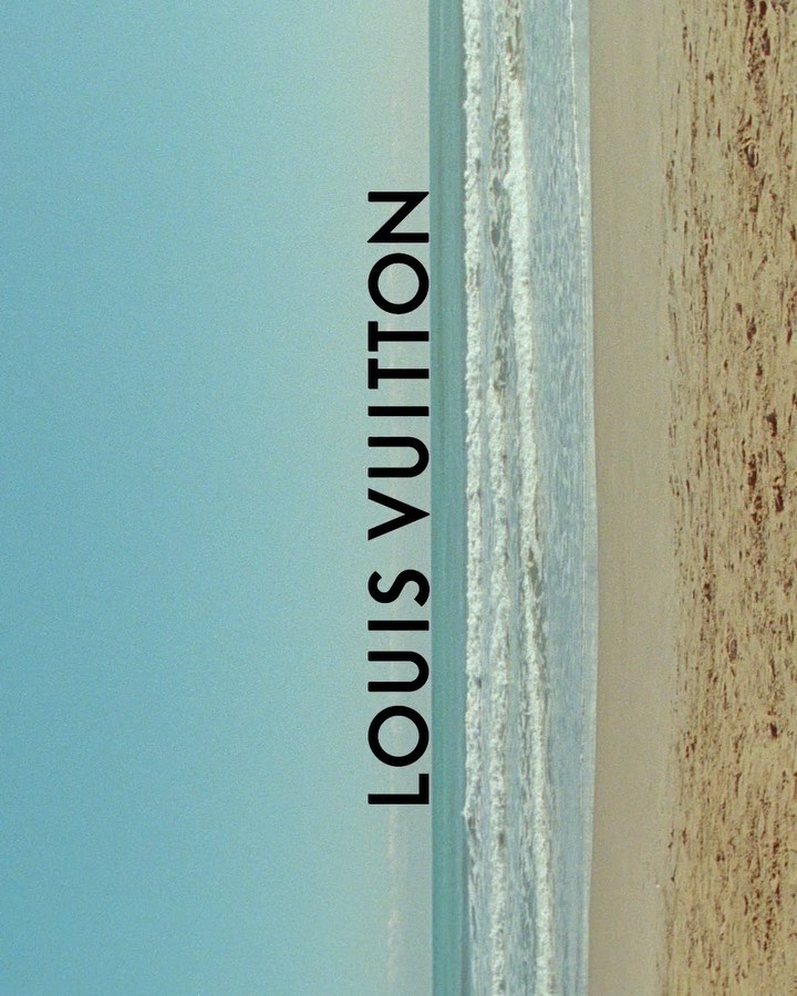 Beach scene with waves washing ashore on tan sand under a clear blue sky, featuring vertical text overlay of the Louis Vuitton brand.