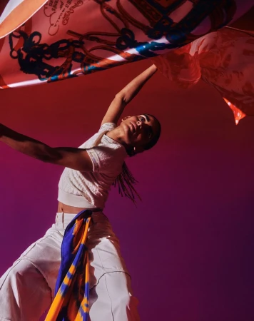 Model holding patterned silk scarves overhead against a gradient red and purple studio background.