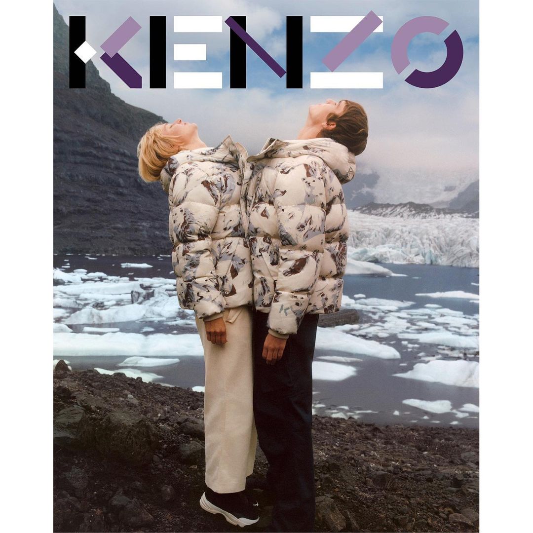 Two models in Kenzo puffer jackets stand back-to-back against a glacial landscape, branded with the KENZO logo, stylish fashion outdoor.