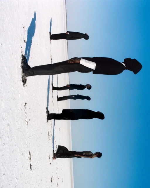Five men in suits stand in a line on a white surface under a blue sky; a creative perspective that plays with scale and landscape.