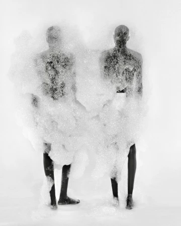 Two figures are nearly obscured by a cloud of white foam in a black-and-white studio photograph with a bright white background.