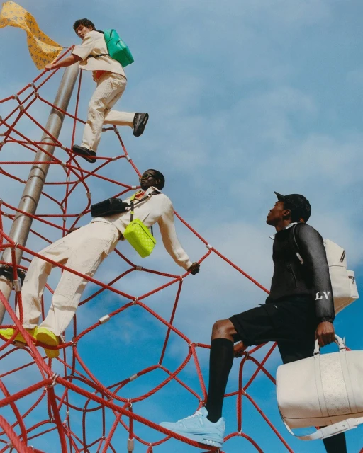 Three men climb a red rope structure in an outdoor setting, showcasing luxury branded bags and clothing against a blue sky backdrop.