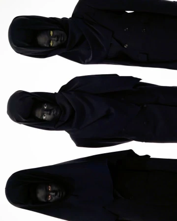 Three hooded figures with darkened skin and striking eyes are stacked vertically against a white background in a studio shot.