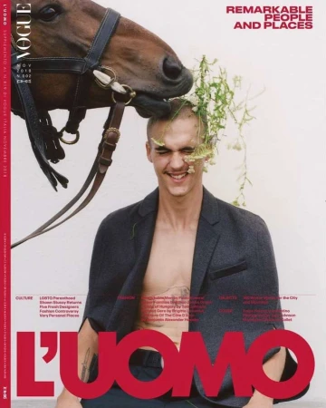 Man smiling with flowers tucked in his hair and a horse nuzzling his head against a white background