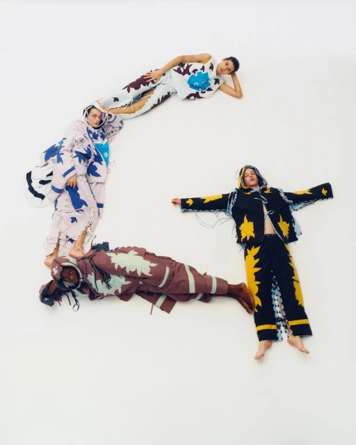 Four models in patterned outfits lying on a white background, arranged to suggest a letter, showcasing fashion and creative posing.