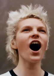 Close-up portrait of a white person with short blonde spiky hair and dental braces shouting, shot by Tom Johnson.