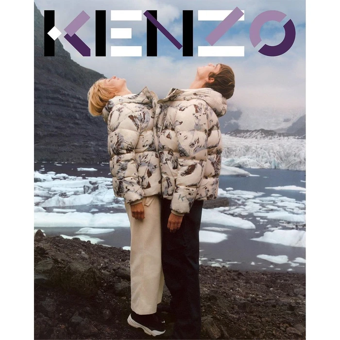 Two models wearing patterned puffer jackets standing back to back looking up in a rugged landscape with glaciers