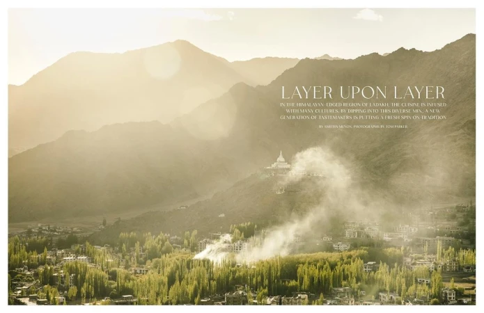 Scenic landscape photography of a village nestled in a valley surrounded by mountains with sunlight and mist creating an ethereal effect.