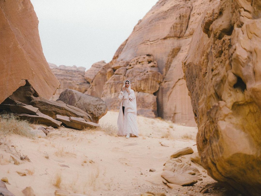 Woman in modest fashion walking through rocky desert landscape with sandstone formations in soft, natural light. Travel and tourism concept.