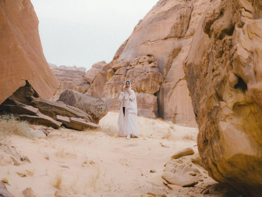 Woman in modest fashion walking through rocky desert landscape with sandstone formations in soft, natural light. Travel and tourism concept.