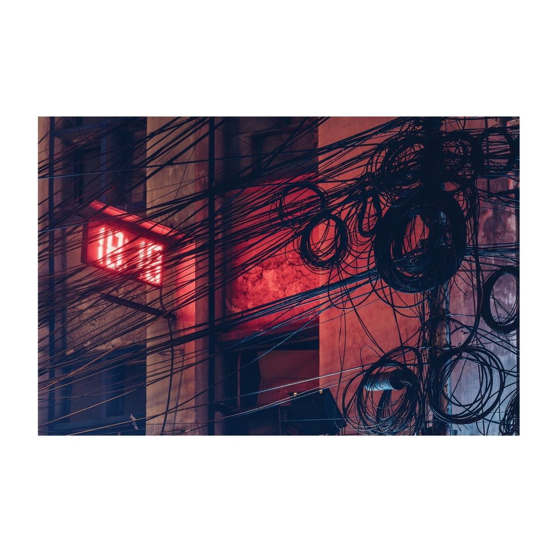 Exterior shot of an urban building with a prominent digital clock and a dense network of tangled wires against a brick wall.