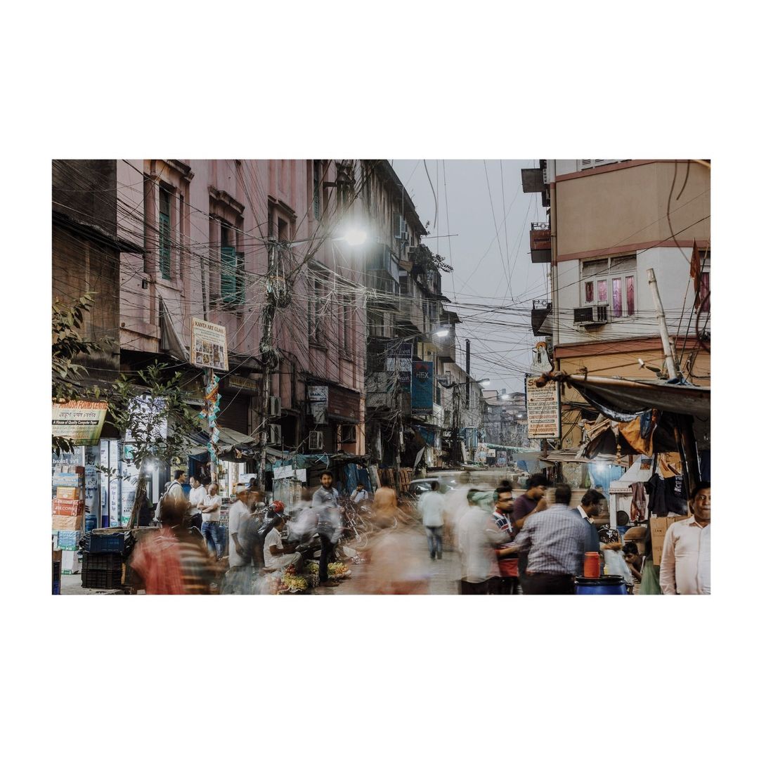 Busy street scene with blurred motion of people and vehicles in an Asian city with aged buildings and overhead electrical wires.